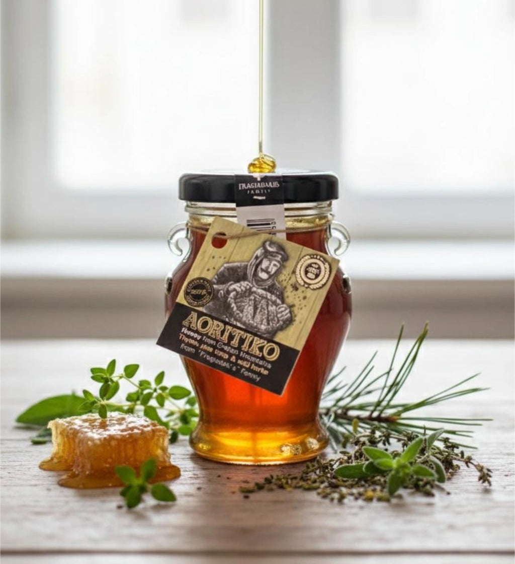 Greek-labeled jar of Cretan thyme honey beside a piece of honeycomb and fresh herbs