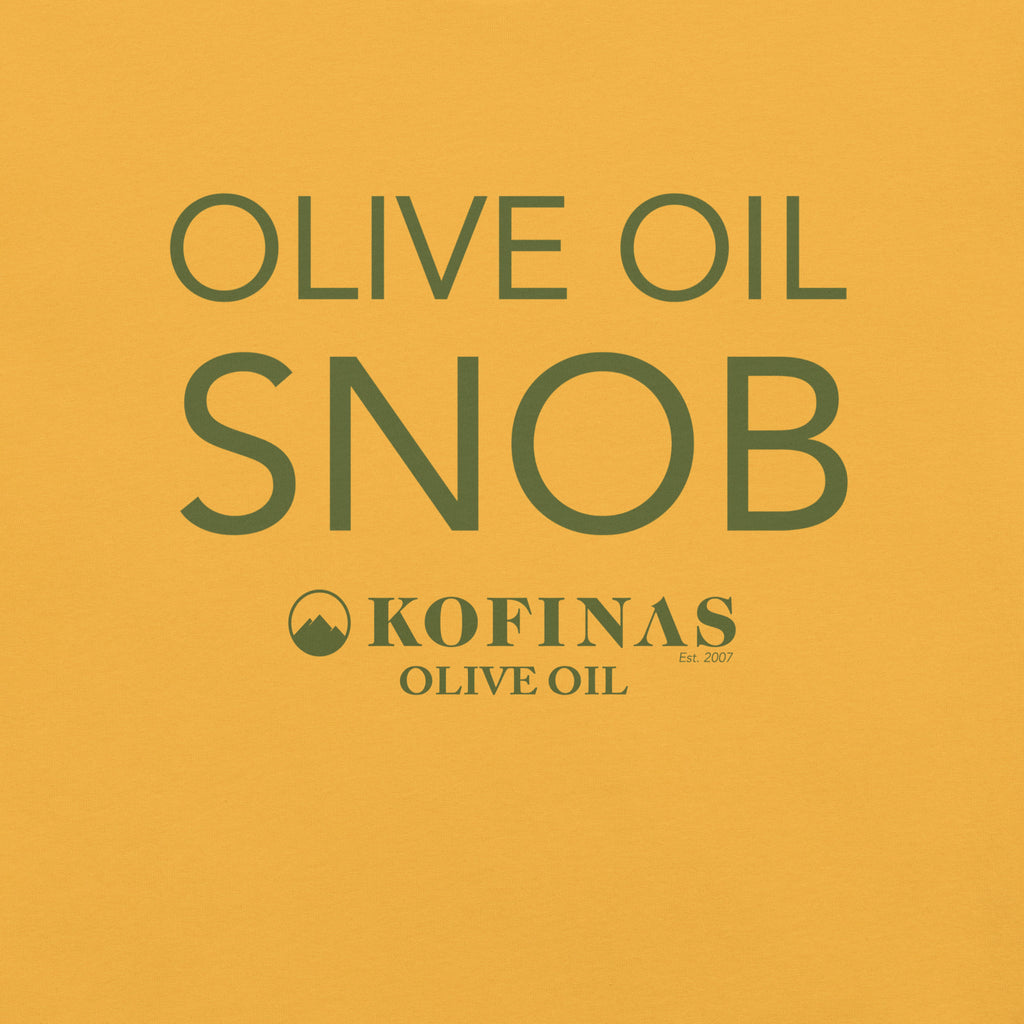 Close-up of a yellow-gold t-shirt printed with 'Olive Oil Snob' and the Kofinas logo